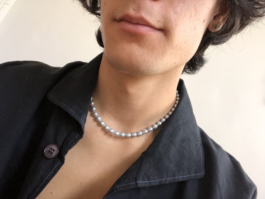 A close-up selfie of Morgan Vo, from below the nose to just below the chest. His hair is mid-length, his dark navy shirt is open, and around his neck is a string of blue-tinted pearls.